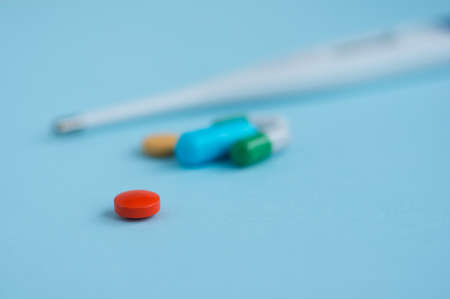 Red pill on a blue background and other medicines and a thermometer in the background