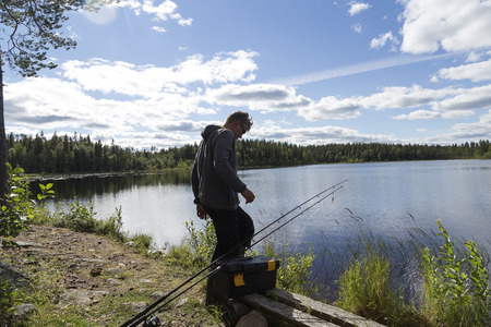 A person standing in front of a lake with two rods and a cloudy skyの写真素材