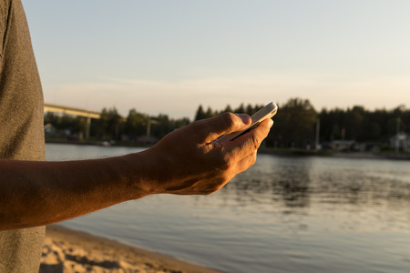 A phone in a mans hand in front of a riverの写真素材