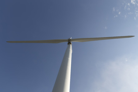 A wind turbine from below with some small clouds on the sky