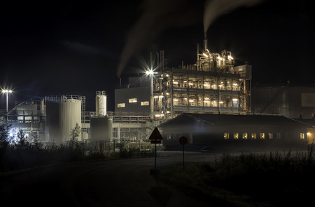 A factory building at night with smoke from the chimneyの写真素材