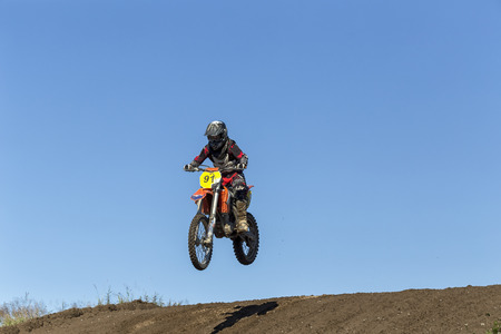 A motorcycle and rider jumping over an obsticle and a clear blue sky in the backgroundのeditorial素材