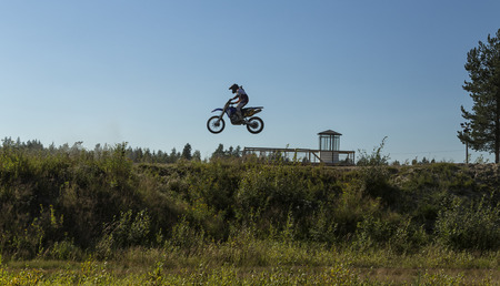 A motorcycle rider jumping from the side with some vegetation in the foregroundのeditorial素材