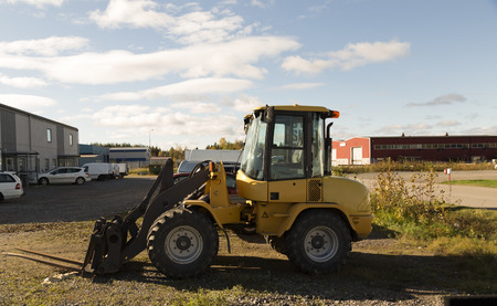 A small tractor parked with a blue sky with some clouds in the background, some cars in front of a...