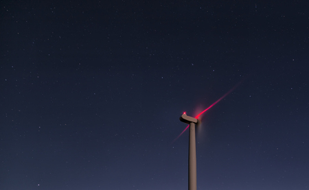 A wind turbine in the night. Sky full of stars and some red light from the warning system reflecting...