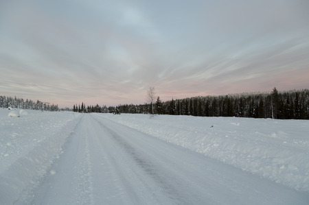 A winter road with a lot of snow and a forest in the backgroundの写真素材