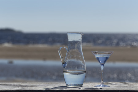 A jug and a glass with water in front of the oceanの写真素材