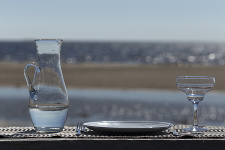 A table with a plate, fork, knife and a glass at the reflecting oceanの写真素材