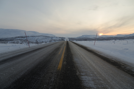 A long road in a winter scene with a sunset in the backgroundの写真素材
