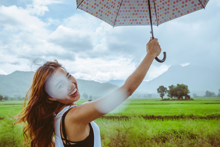 Asian women travel relax in the holiday. Women stand in rain umbrellas. On the meadow During the rainy season.Thailandの写真素材