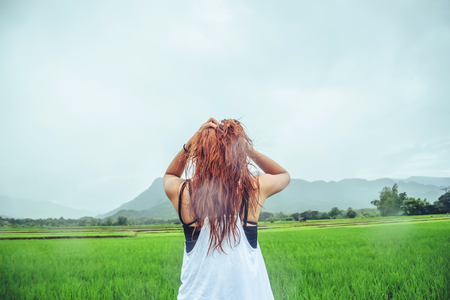 Asian women travel relax in the holiday. Stand in a meadow in the rain. On the meadow During the rainy season.Thailandの写真素材