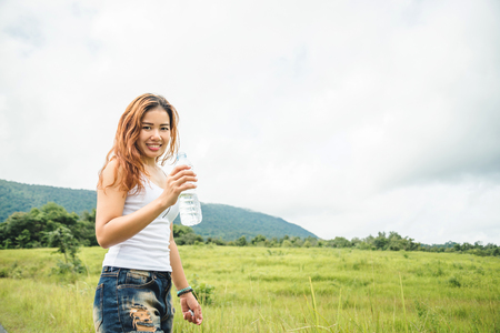 Asian women travel relax in the holiday. Drink Water on a green pasture.の写真素材