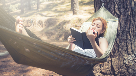 Sleeping women write notes. In the hammock. In the natural atmosphere in the parkの写真素材