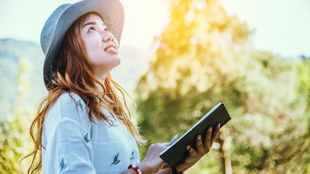Asian woman travel nature. Travel relax. Study read a book. Nature Education Write a note At public park in summer. In Thailandの写真素材