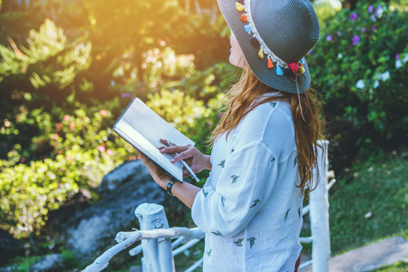 Asian woman travel nature. Travel relax. Study read a book. Nature Education Write a note At public park in summer. In Thailandの写真素材