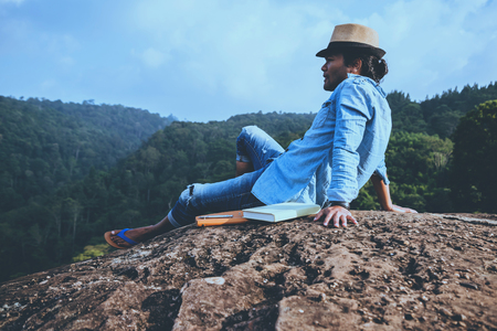 Asian man travel relax in the holiday. seats relax read books on rocky cliffs. On the Moutain summer. In Thailandの写真素材