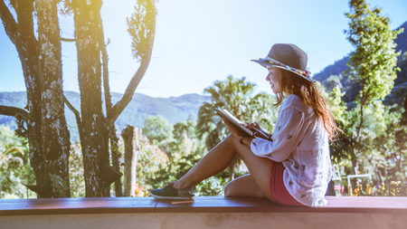 Asian woman travel nature. Travel relax. Study read a book. Nature Education Write a note At public park in summer. In Thailandの写真素材