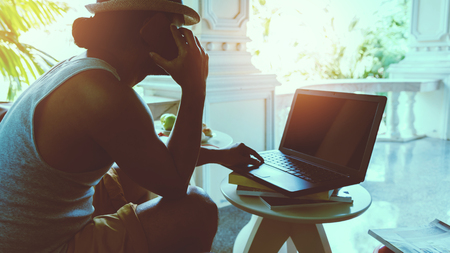 Man is working sitting on the sofa. Hands are holding mobile phone and  working with a notebookの写真素材