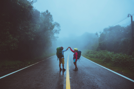 Lover asian man and asian women travel nature. Walk on the road route. traveling nature happily. Amid the mist rainy. in the rainy season.の写真素材