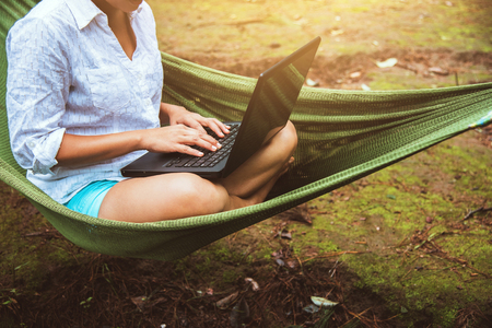 Women travel in natural sitting in the hammock and working in a natural park using a notebook.の写真素材