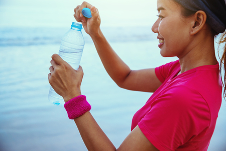 Asian women jogging workout on the beach in the morning. Relax with the sea walk and drinking water from the plastic bottlesの写真素材