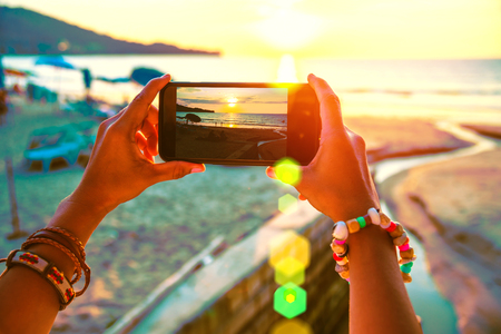 Asian woman travel nature. Travel relax. Use cell phone take pictures the sunset on the beach. In the summerの写真素材