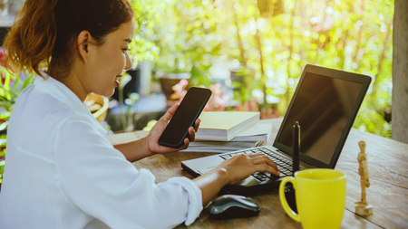 asian woman sitting at table. sitting working in the holiday is laptop, smartphone and cup of coffee.On computer screen.の写真素材