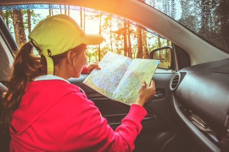 Asian women travel relax in the holiday. Traveling by car park. View map for Nature tours during the rainy season.の写真素材
