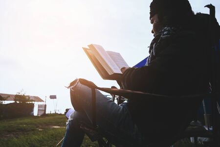 Asian man travel relax in the holiday. camping on the Mountain. sit read a book on the chair. Thailandの写真素材