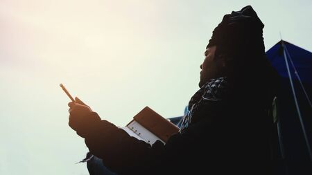 Asian man travel relax in the holiday. camping on the Mountain. sit write a note on the chair. Thailandの写真素材