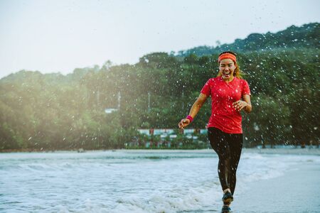 asian woman jogging workout on the beach in the morning. Relax with the beach. fun and happy with playing, jumping, kicking the sea. in summerの写真素材