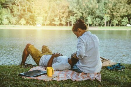 Asian couple lover sitting a relax River side in the public park. working with a notebook and drinking coffee.in the park. in the holiday.の写真素材