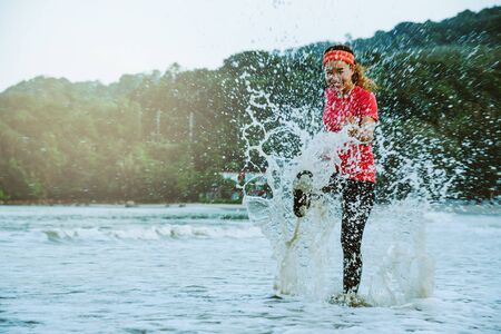 asian woman jogging workout on the beach in the morning. Relax with the beach. fun and happy with playing, jumping, kicking the sea. in summerの写真素材