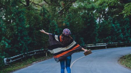 Young woman travel nature. She walking on asphalt road in forest pine green and write a note among the pine trees enjoying nature.の写真素材