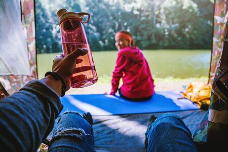 Young man submitting a bottle of drinking water to lover at camping tent facial.の写真素材