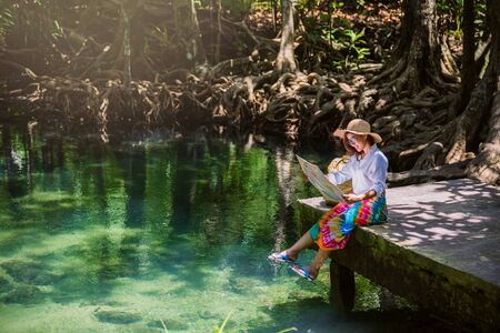Asian women travel relax, travel nature in the holiday. women enjoying Sitting and watching the travel map the lake mangrove forest. tha pom-klong-song-nam at krabi. summer, Mapの写真素材