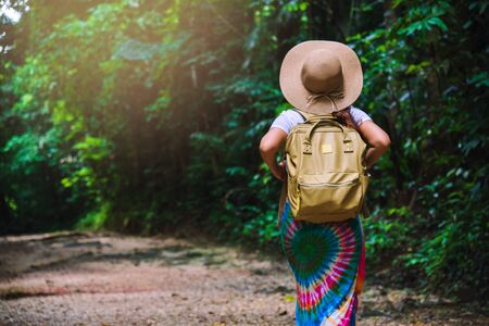 Young girl with backpack enjoying  travel nature in the forest Lush green trees. The back view of the girl who is walking travel in the forest. In the summer, Travel relax, Travel Thailand.の写真素材