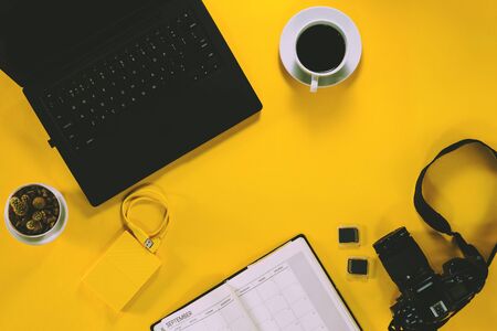Conceptual workspace, Laptop computer and coffee cup, note book with Camera and Cactus tree. External hard disk with USB on pastel background yellow. Top view. Flat lay. summerの写真素材