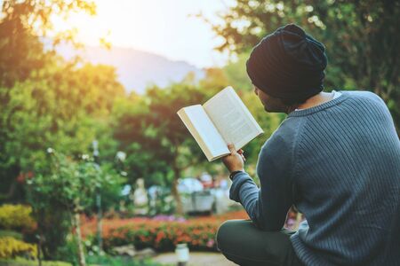 The young man travels nature on the mountain, is sitting and relaxing, reading a book in the flower garden.の写真素材