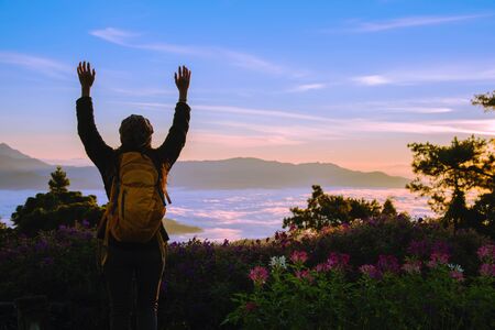 Young woman Tourists with backpacks Standing watching nature beautiful landscape view And fog on the top of the mountain Morning sunrise.の写真素材