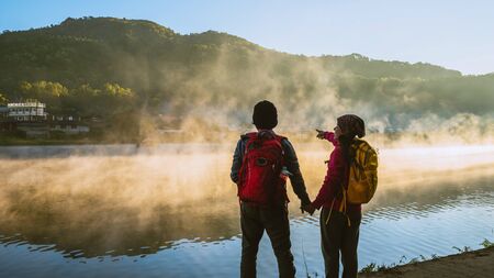 Asian woman and Asian man which backpacking standing near the lake, she was smiling, happy and enjoying the natural beauty of the mist.の写真素材
