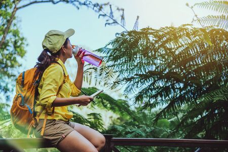 The young woman travels recording and studying the nature of the forest. She is sitting, relaxing and drinking water.の写真素材