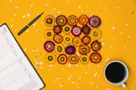 Top view concept of pastel yellow background. Colorful flowers that are arranged shape with a notebook pen and Cup of coffee placed.の写真素材
