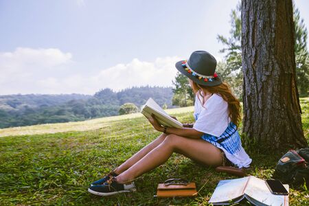 Asian woman travel nature. Travel relax. Girl sitting reading a book Under the tree. Beautiful girl in autumn forest reading a book Nature Education and Write a note.の写真素材