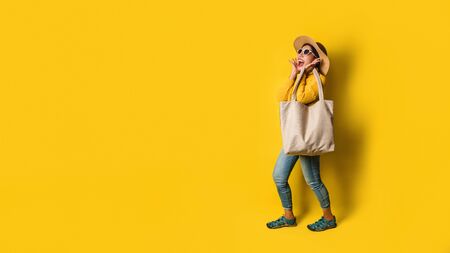 Portrait of an excited beautiful girl wearing dress and sunglasses holding shopping bags. Cheerful young woman with handbag on yellow background. Shopaholic shopping Fashion.の写真素材