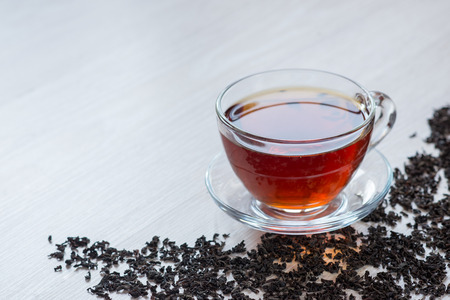 Black tea in a transparent glass bowl on a table. Dry black tea scattered on the table.の写真素材