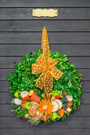 Spring wreath with orange bow hanging on dark wooden door with name plateの写真素材