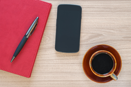 Coffee cup, smartphone and notebook with pen on wood deskの写真素材