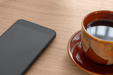 Coffee cup and smartphone on wood deskの写真素材