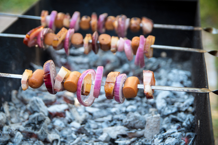Shashlik with frankfurter, bacon and onion laying on the grillの写真素材